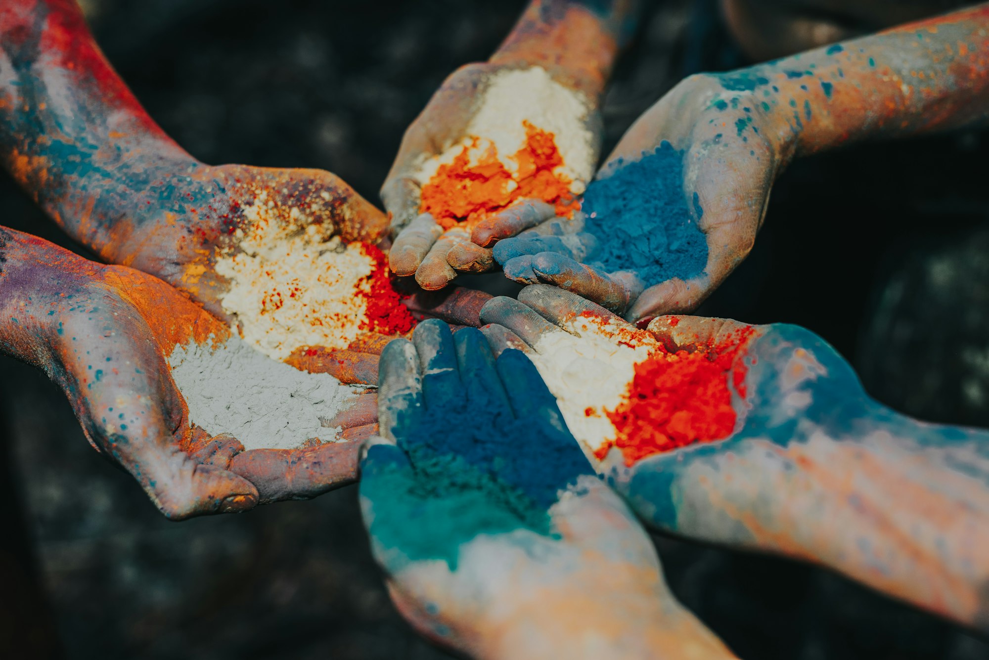 Hands holding bright Holi colour powders in orange, blue and white