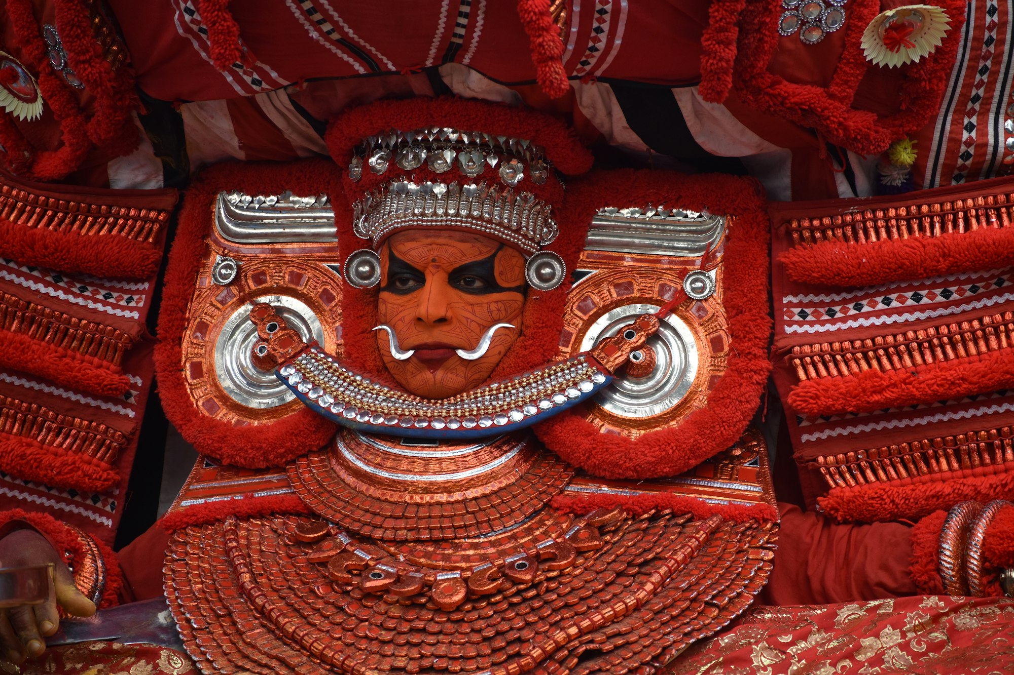 A theyyam performer in red and gold headdress and face paint, North Kerala
