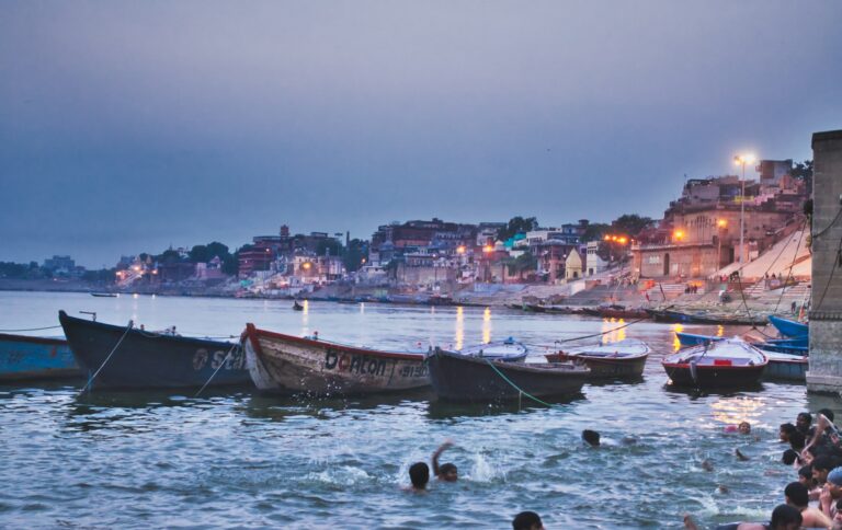 Wooden boats moored on the Ganges below the lit ghats of Varanasi at dusk